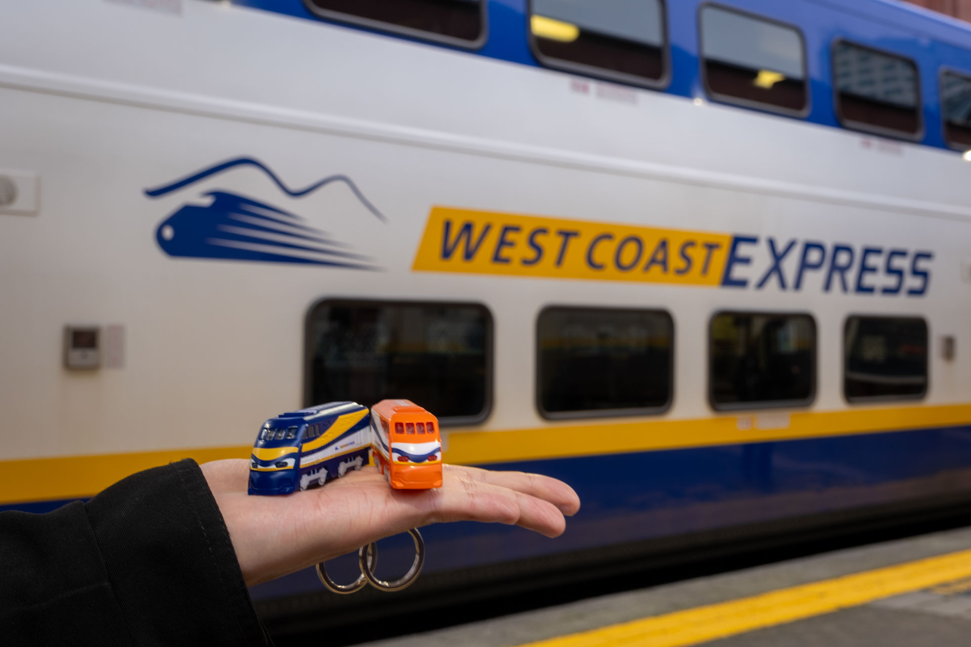 A person holds up the Compass Mini-WCE on their palm in front of a West Coast Express car