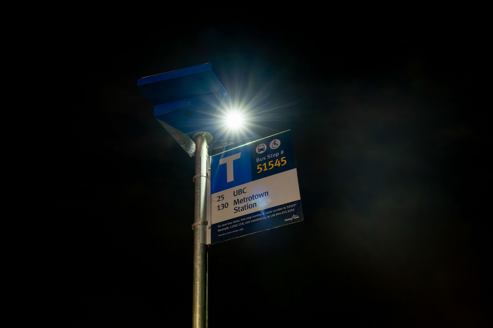A bus stop is illuminated by the light on top.