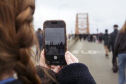 A person holds up a smartphone to take a photo of the Pattullo Bridge while standing on the bridge deck