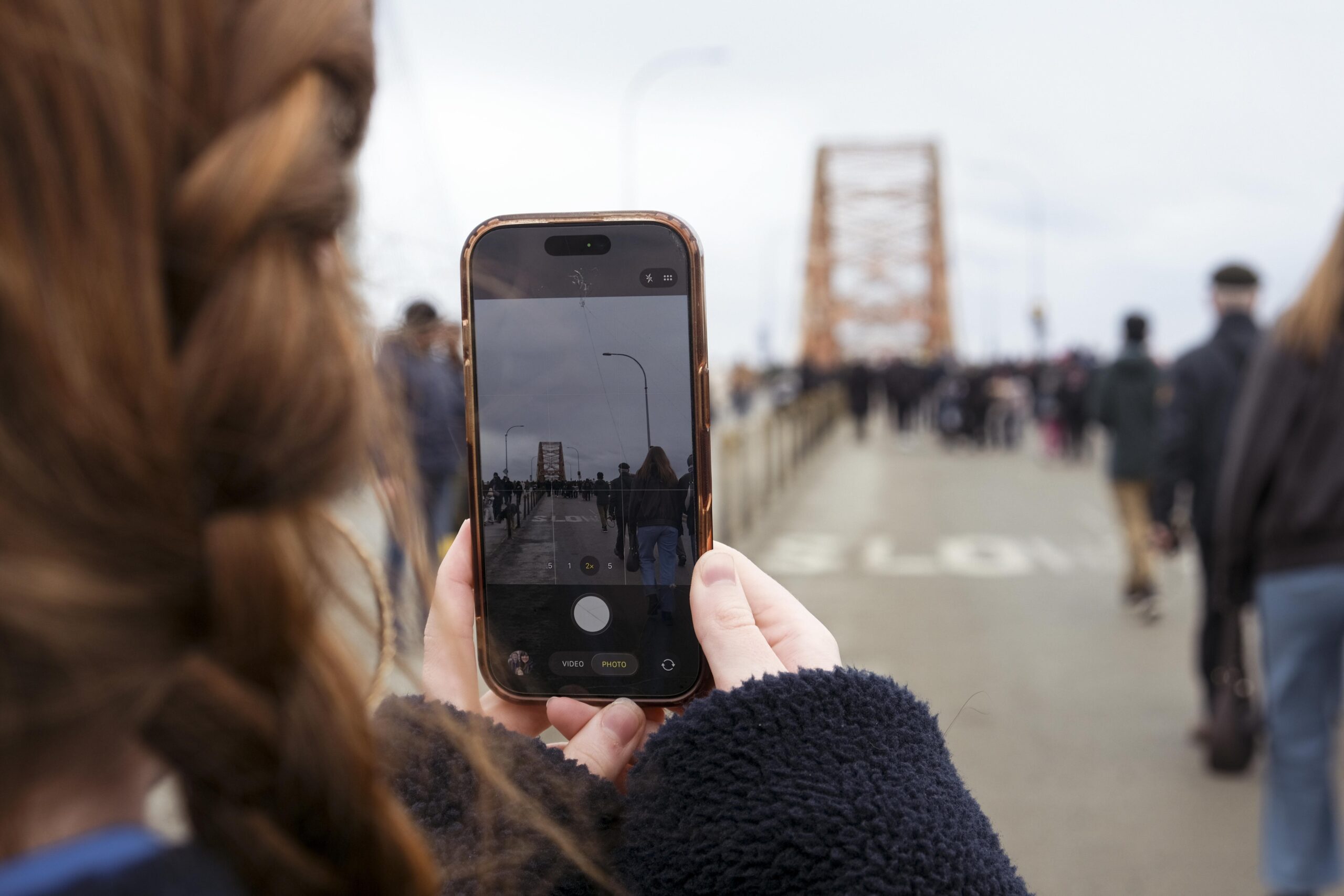A person holds up a smartphone to take a photo of the Pattullo Bridge while standing on the bridge deck