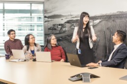 TransLink staff seated around a conference table during a meeting, with one team member presenting while others listen and work on laptops.