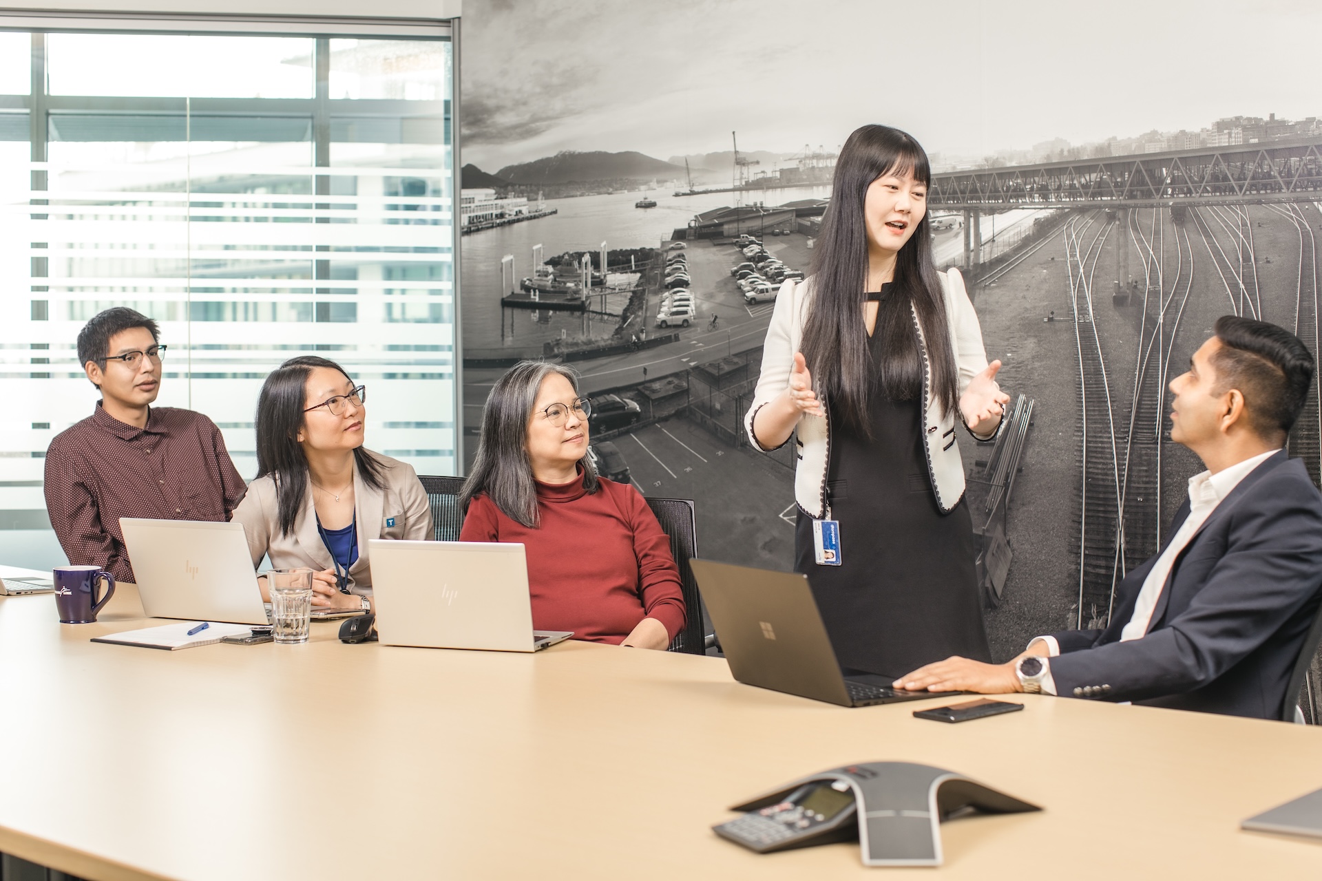 TransLink staff seated around a conference table during a meeting, with one team member presenting while others listen and work on laptops.